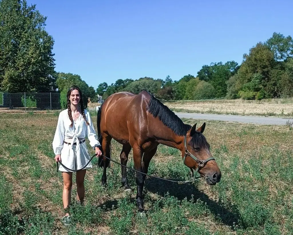 Zertifizierte Tierenergetikerin Romaine lächelnd mit einem braunen Pferd auf einer grünen Wiese – Symbolbild für energetische Tiertherapie in Luzern
